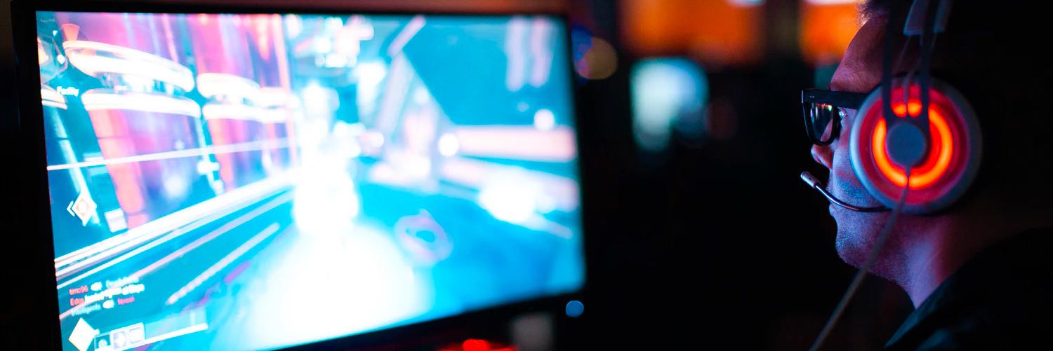 A PC gamer at a bright monitor wearing a lit gaming headset